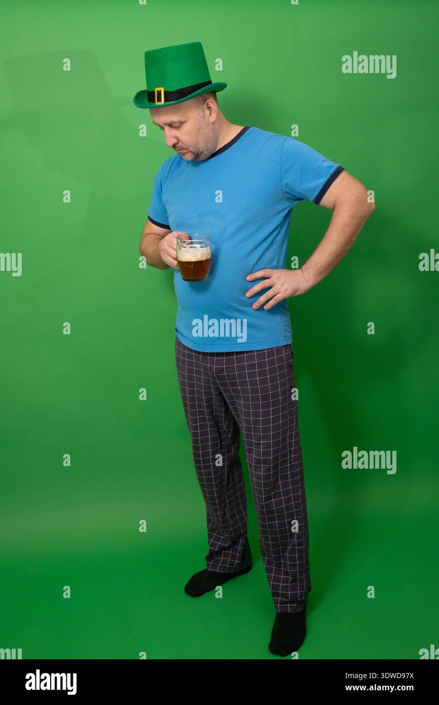 Homme portant un chapeau de leprechaun vert et tenant une tasse de bière mousseuse sur fond vert. – Concept de vacances Patricks Day avec célébration irlandaise et tradition pub. photographie Banque D'Images