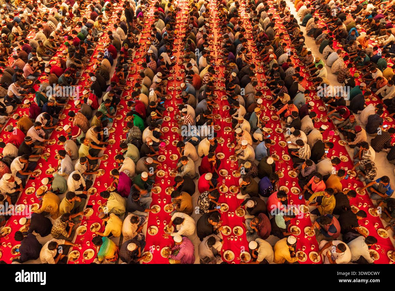 Dhaka, Bangladesh - 25 février 2026 : vue aérienne de rangées sur rangées de personnes assises à iftar, une mer de têtes et de mains contre la table rouge vibrante Banque D'Images