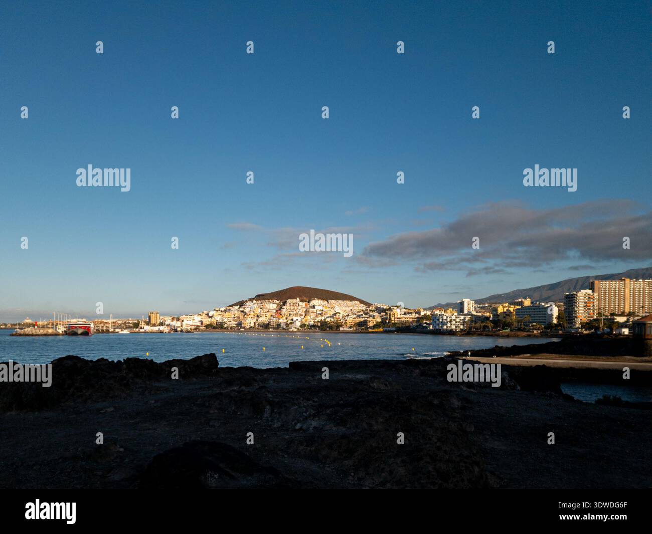 Lumière tôt le matin illuminant la ville côtière de Los Cristianos à Tenerife, avec des eaux calmes de l'océan et un ciel bleu clair créant un bord de mer paisible Banque D'Images