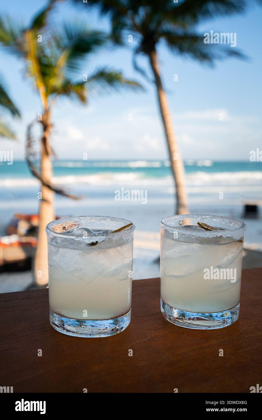 Deux cocktails rafraîchissants sont assis sur une table en bois près de la magnifique plage de Tulum au Mexique. Les palmiers balancent en arrière-plan, et les vagues de l'océan doucement l Banque D'Images