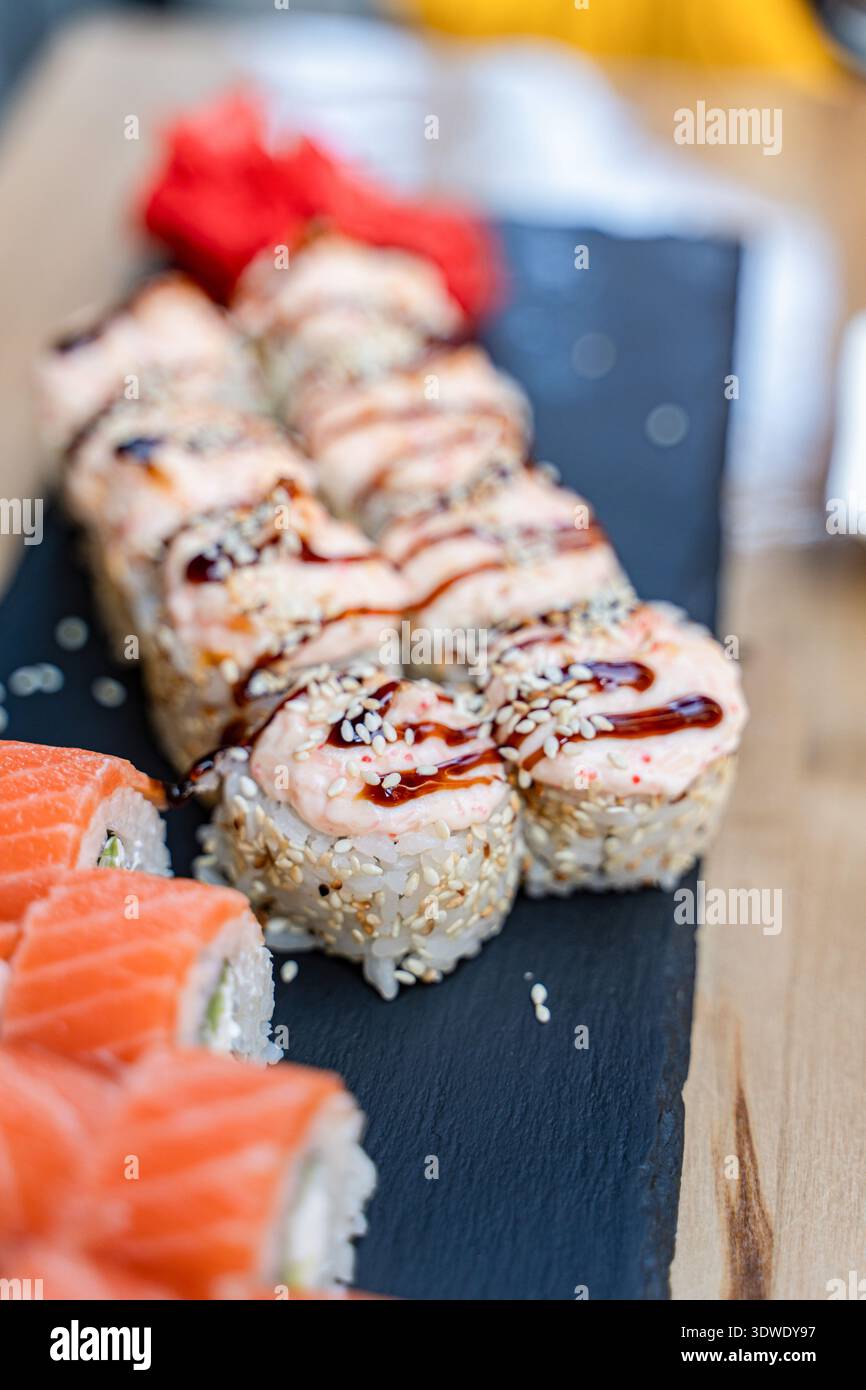 Assortiment de rouleaux de sushi, avec saumon et diverses garnitures, agencés avec art sur un plateau d'ardoise noire. La présentation vibrante met en valeur le frais Banque D'Images