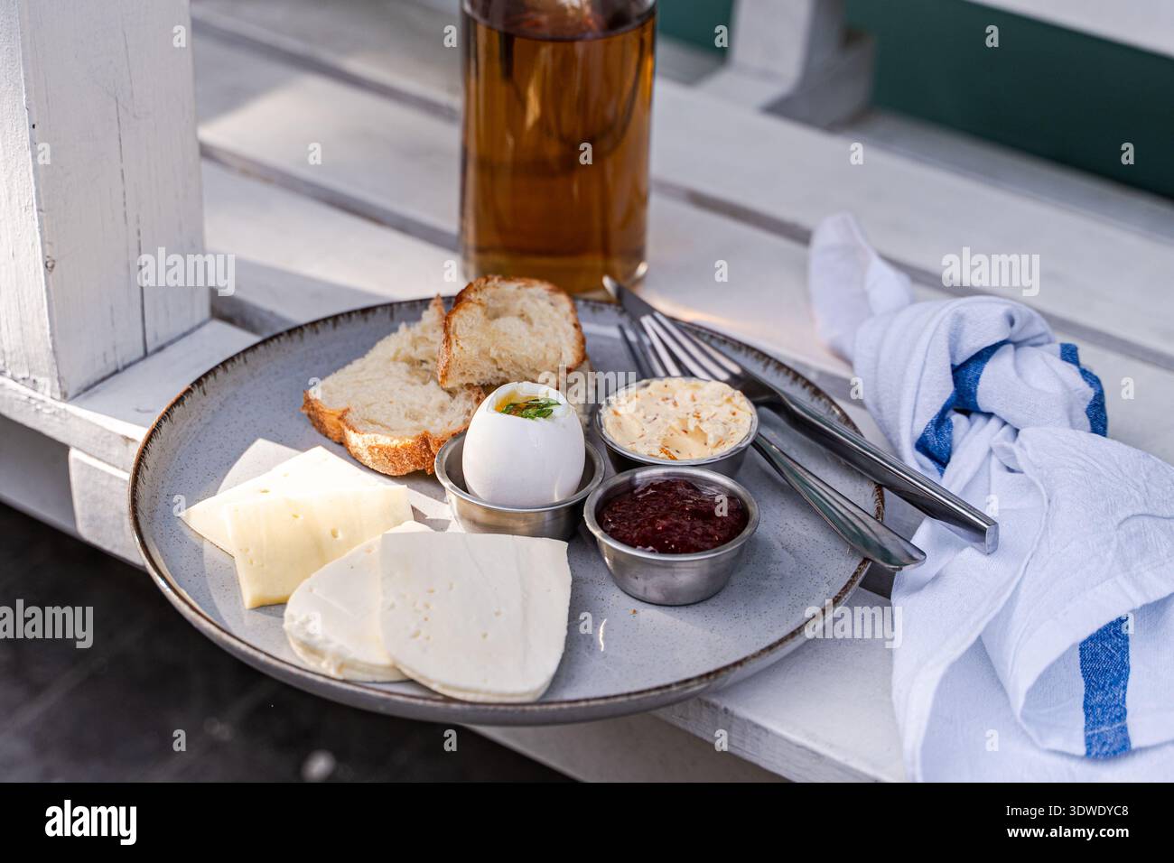 Une assiette de petit-déjeuner avec du fromage tranché, un œuf dur, du pain, du beurre et de la sauce se trouve sur une table. L'arrangement offre un début simple mais délicieux Banque D'Images