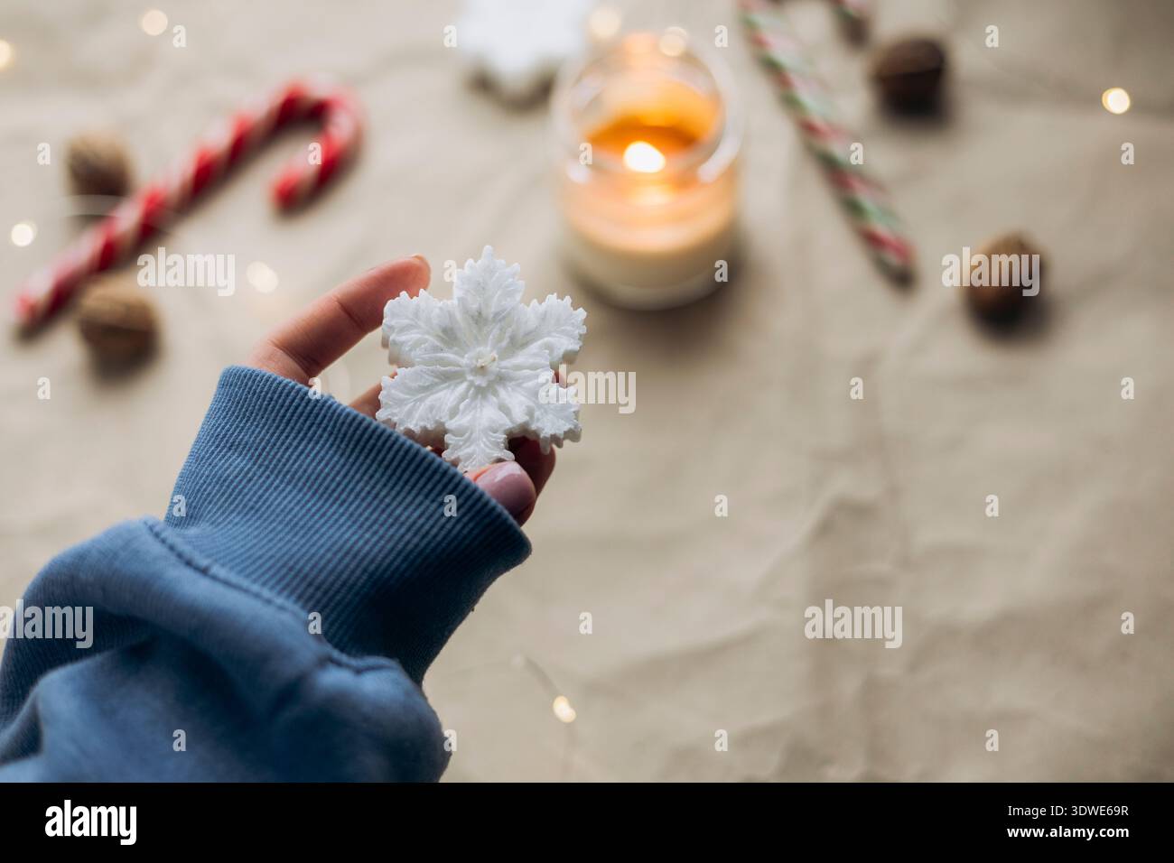 Une main confortable vêtue d'un pull bleu tient un délicat ornement de flocon de neige, capturant l'essence de la saison de Noël festive. Un éclairage doux crée un Banque D'Images