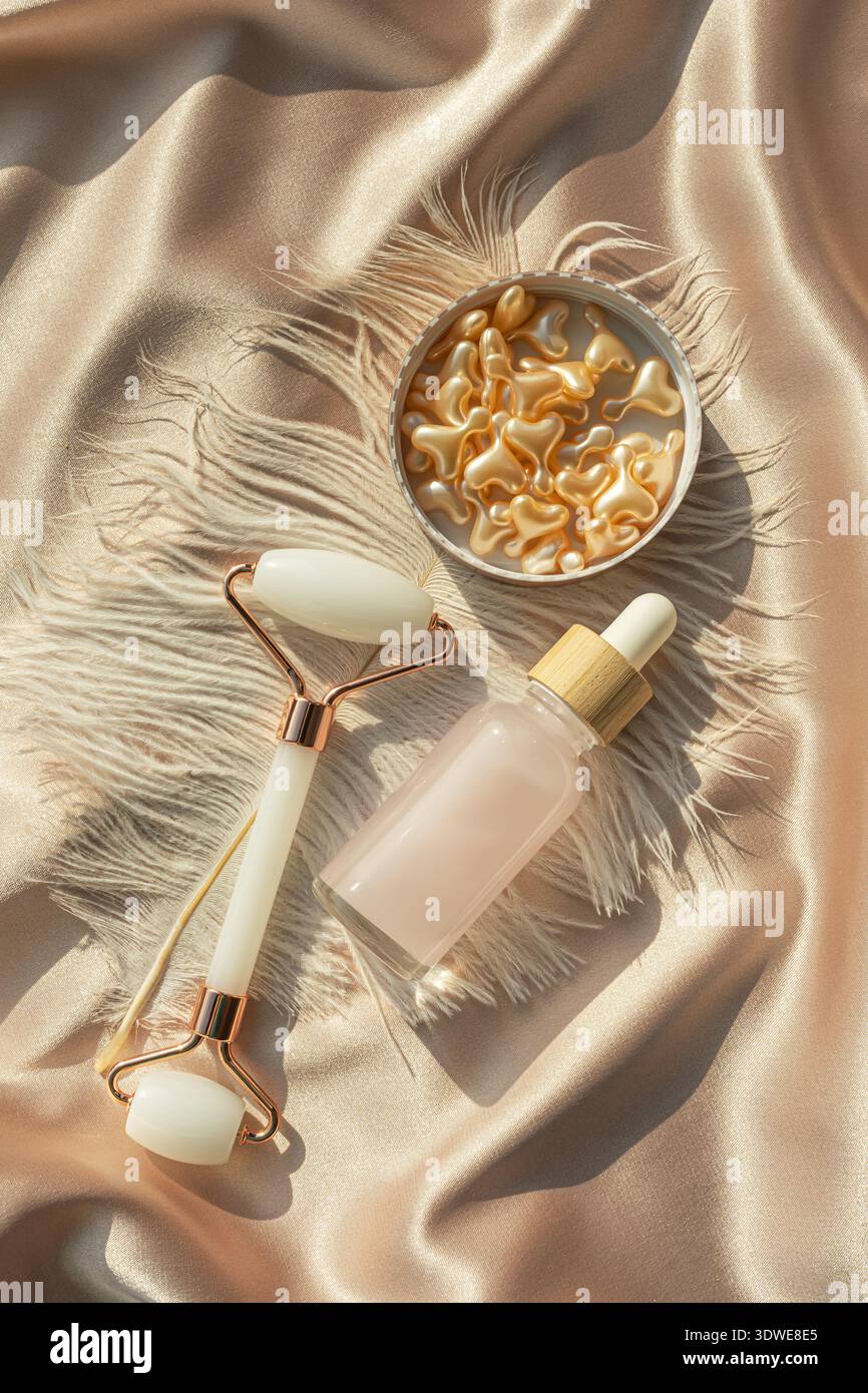 Une luxueuse couche plate d'essentiels de beauté, avec des capsules cosmétiques dorées, un rouleau pour le visage et une bouteille de sérum sur un fond satiné, mettant l'accent sur SK Banque D'Images
