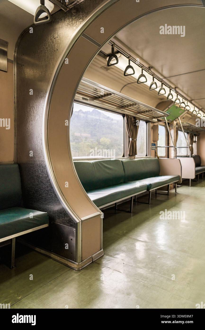 Un intérieur de train vintage à Taiwan, présentant des sièges verts vides et de grandes fenêtres encadrées par des arches métalliques, créant une atmosphère de voyage nostalgique Banque D'Images