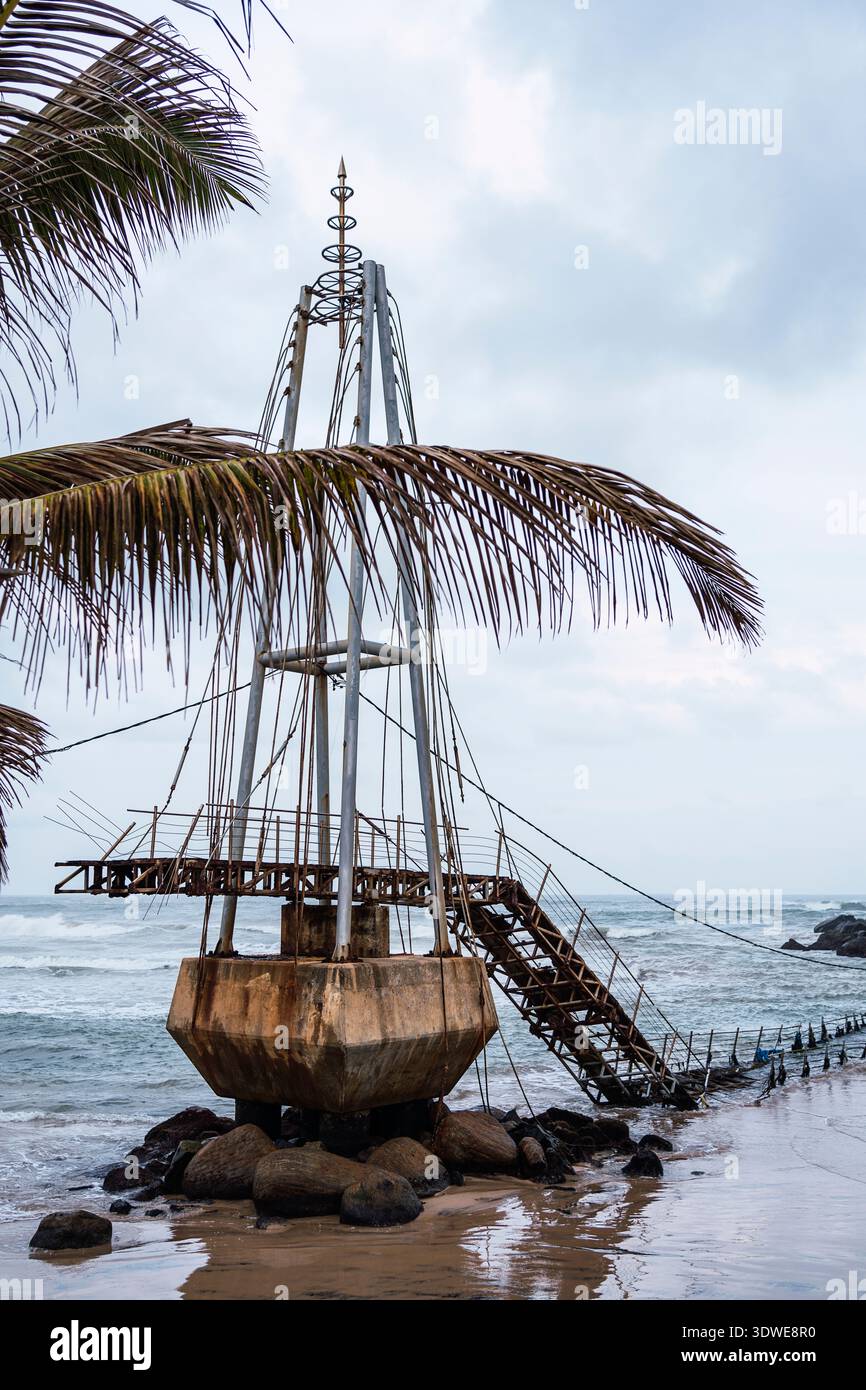 Une structure côtière unique s'élève de la plage de sable, encadrée par un palmier et des vagues de l'océan, dans un cadre serein sur la côte pittoresque du Sri Banque D'Images