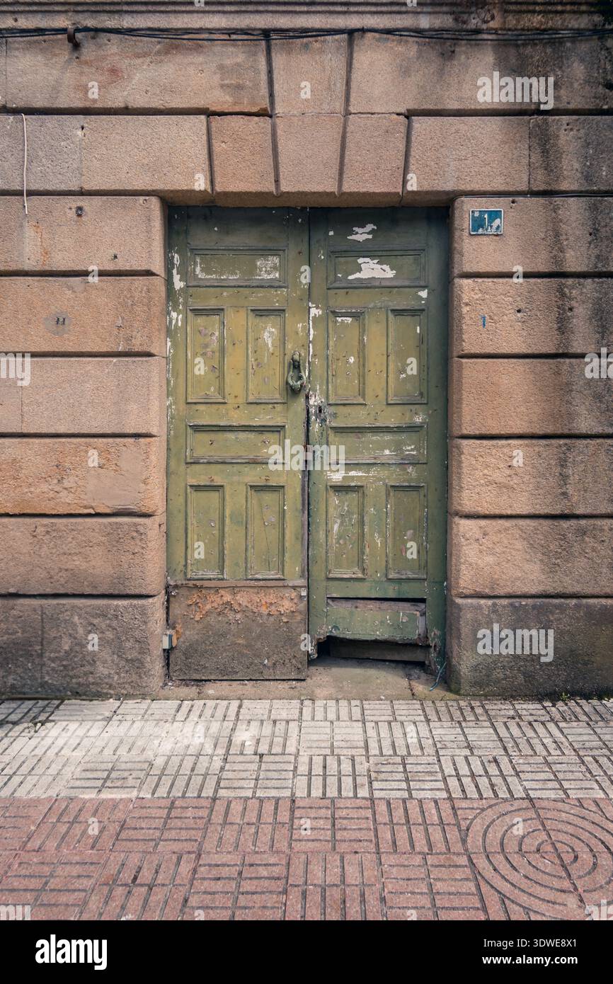 Porte en bois vert altéré sur un bâtiment en pierre à Luarca, Asturies. La façade rustique évoque le charme historique des vacances d'été passées dans ce coas Banque D'Images