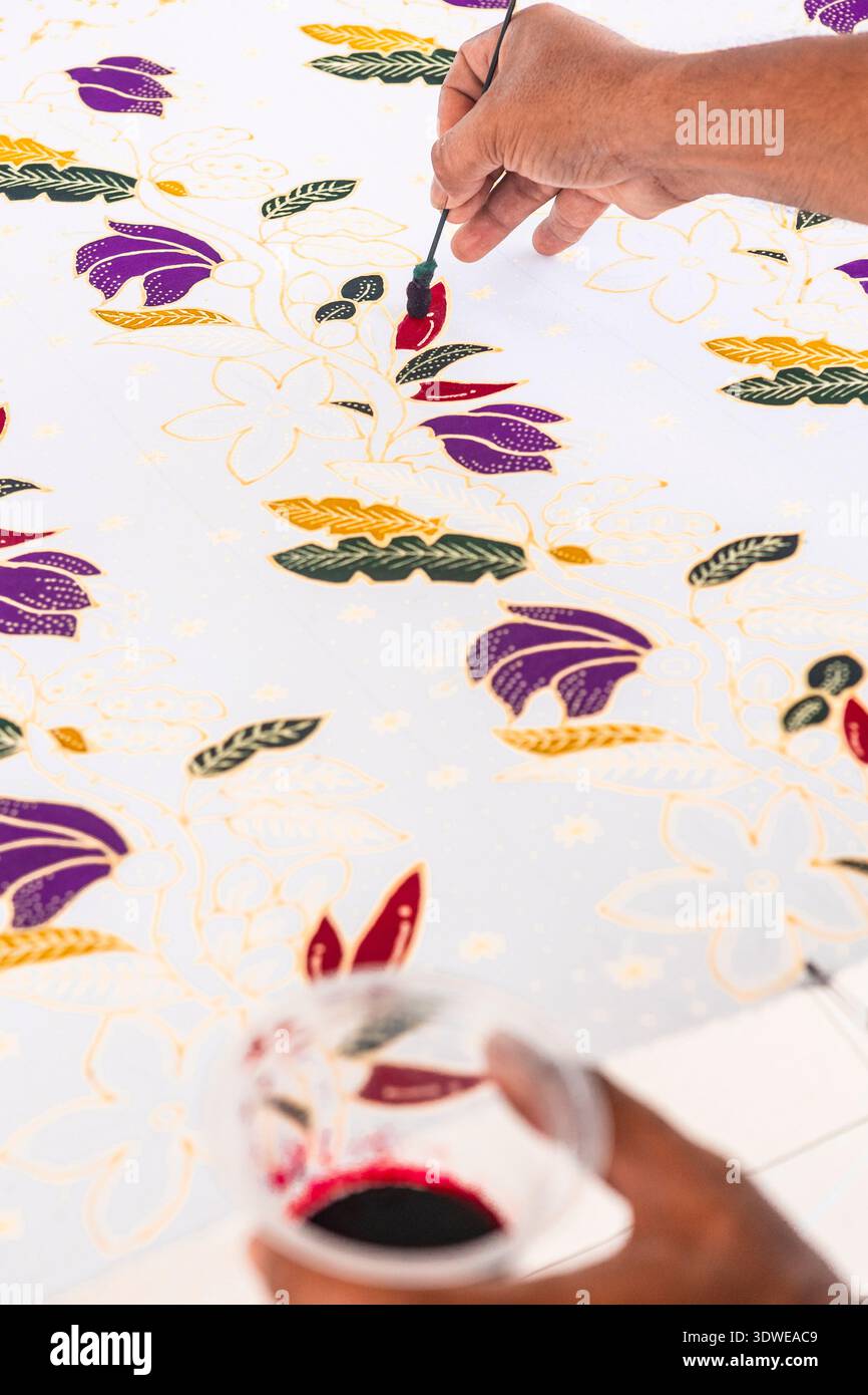 Une vue détaillée d'une main peignant des motifs de batik complexes dans des couleurs vives, mettant en valeur l'artisanat indonésien traditionnel reconnu par l'UNESCO comme Banque D'Images