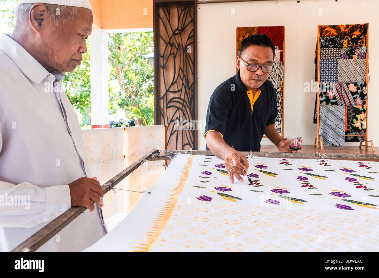 Les artisans indonésiens collaborent sur un design batik traditionnel, peignant soigneusement à la main des motifs vibrants sur le tissu. La technique complexe reflète Banque D'Images