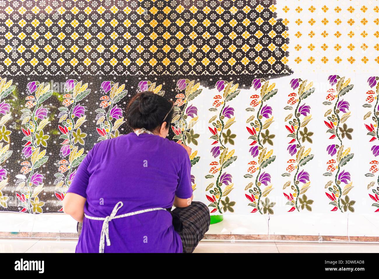 Un artisan indonésien élabore méticuleusement des motifs de batik complexes, un patrimoine culturel immatériel de l'UNESCO, mettant en valeur des motifs floraux vibrants à l'aide de tra Banque D'Images