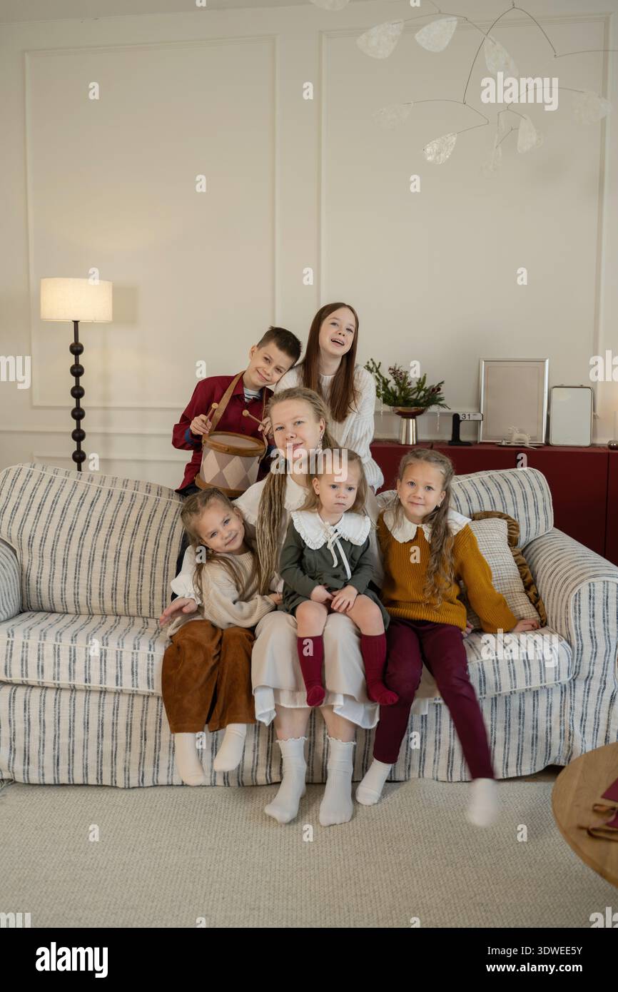 Une famille joyeuse s'est réunie sur un canapé, célébrant Noël à la maison. Les enfants habillés chaleureusement, souriants et liés, créent un guichet automatique de vacances chaleureux et festif Banque D'Images
