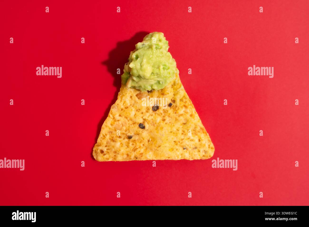 Une seule puce de nacho mexicaine est généreusement recouverte de guacamole crémeux sur un fond rouge vif. Les couleurs vives soulignent la texture appétissante Banque D'Images
