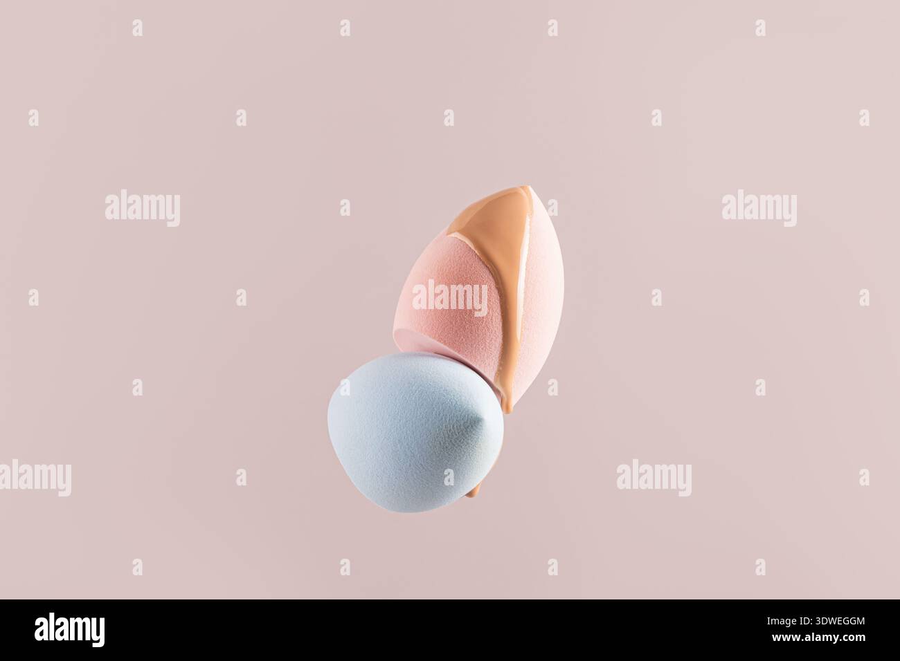 Gros plan d'échantillons de fond de teint liquide beige sur des éponges de maquillage roses et bleues douces sur un fond pastel. Idéal pour la beauté, les cosmétiques et le maquillage co Banque D'Images