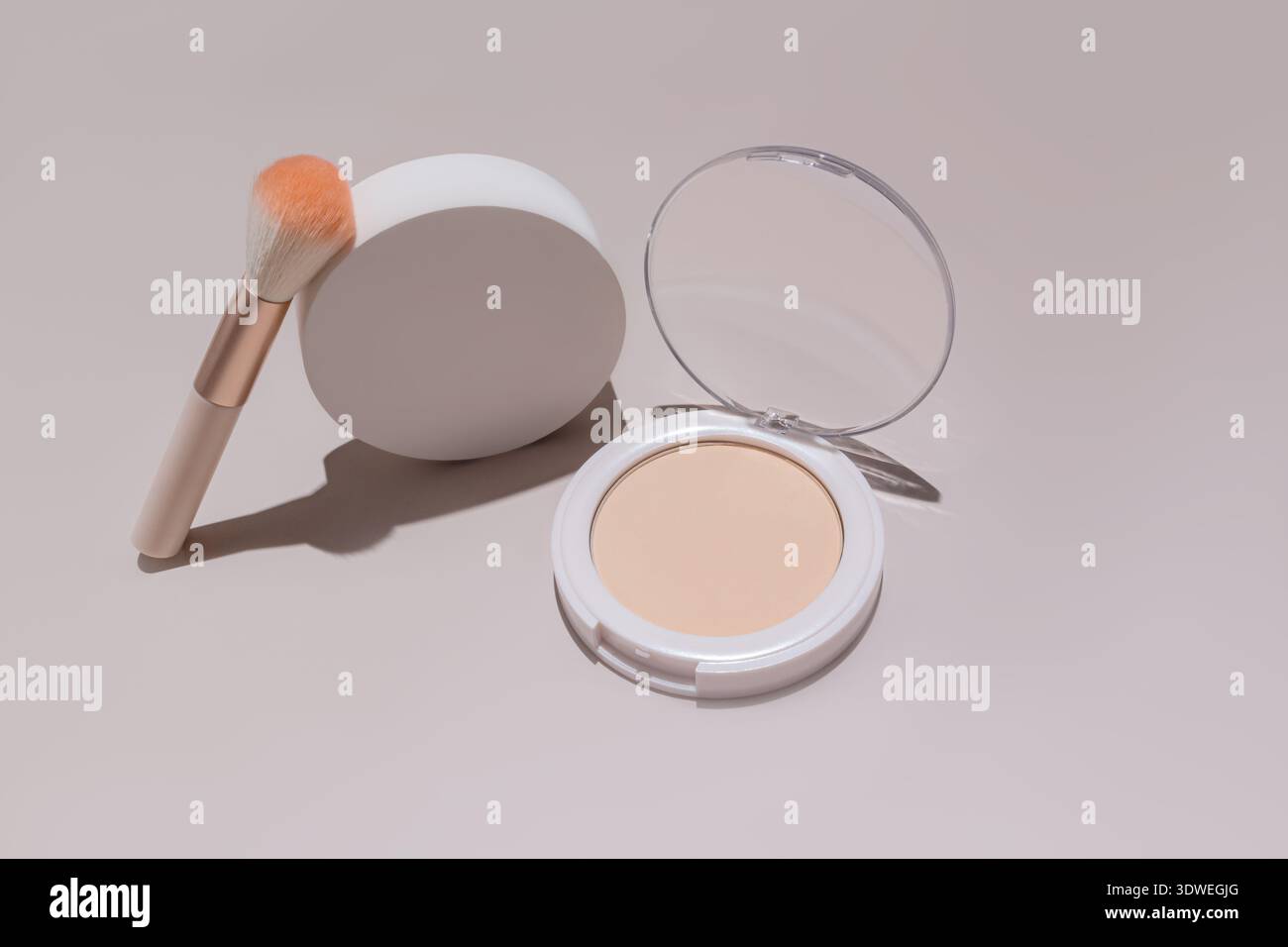 Un étui compact à poudre avec un couvercle transparent est affiché à côté d'une brosse de maquillage. Les tons subtils soulignent son élégance cosmétique, adapté à la beauté et Banque D'Images