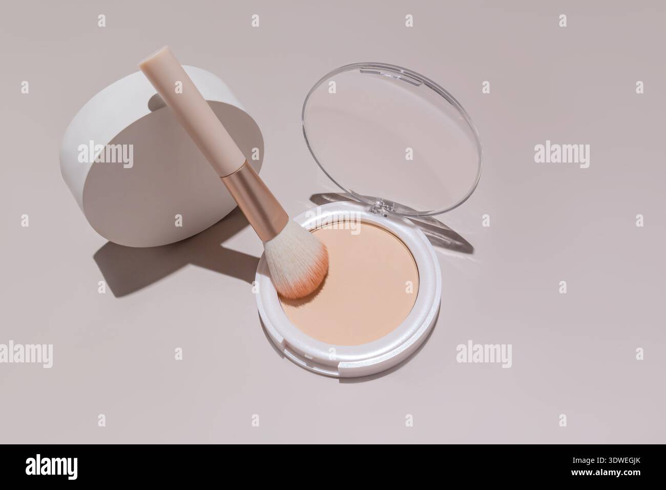 Un étui en poudre compact et élégant avec un pinceau d'application doux sur un fond neutre, offrant un échantillon cosmétique de haute qualité idéal pour la beauté et le maquillage Banque D'Images