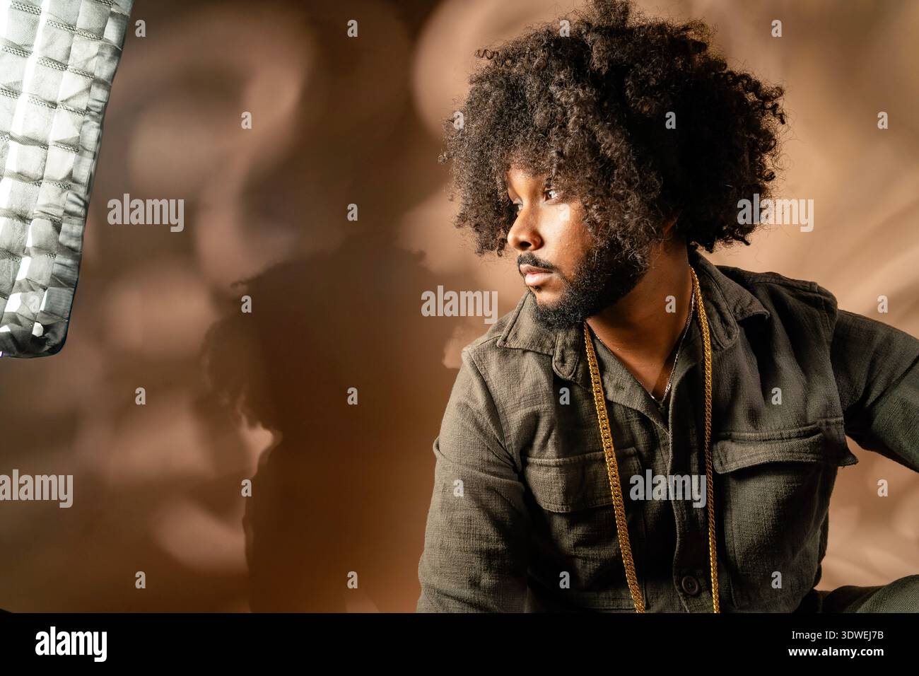 Un homme avec une coiffure afro est capturé dans un studio. Il regarde soigneusement sur le côté, avec un éclairage doux projetant des ombres sur un fond neutre, c Banque D'Images