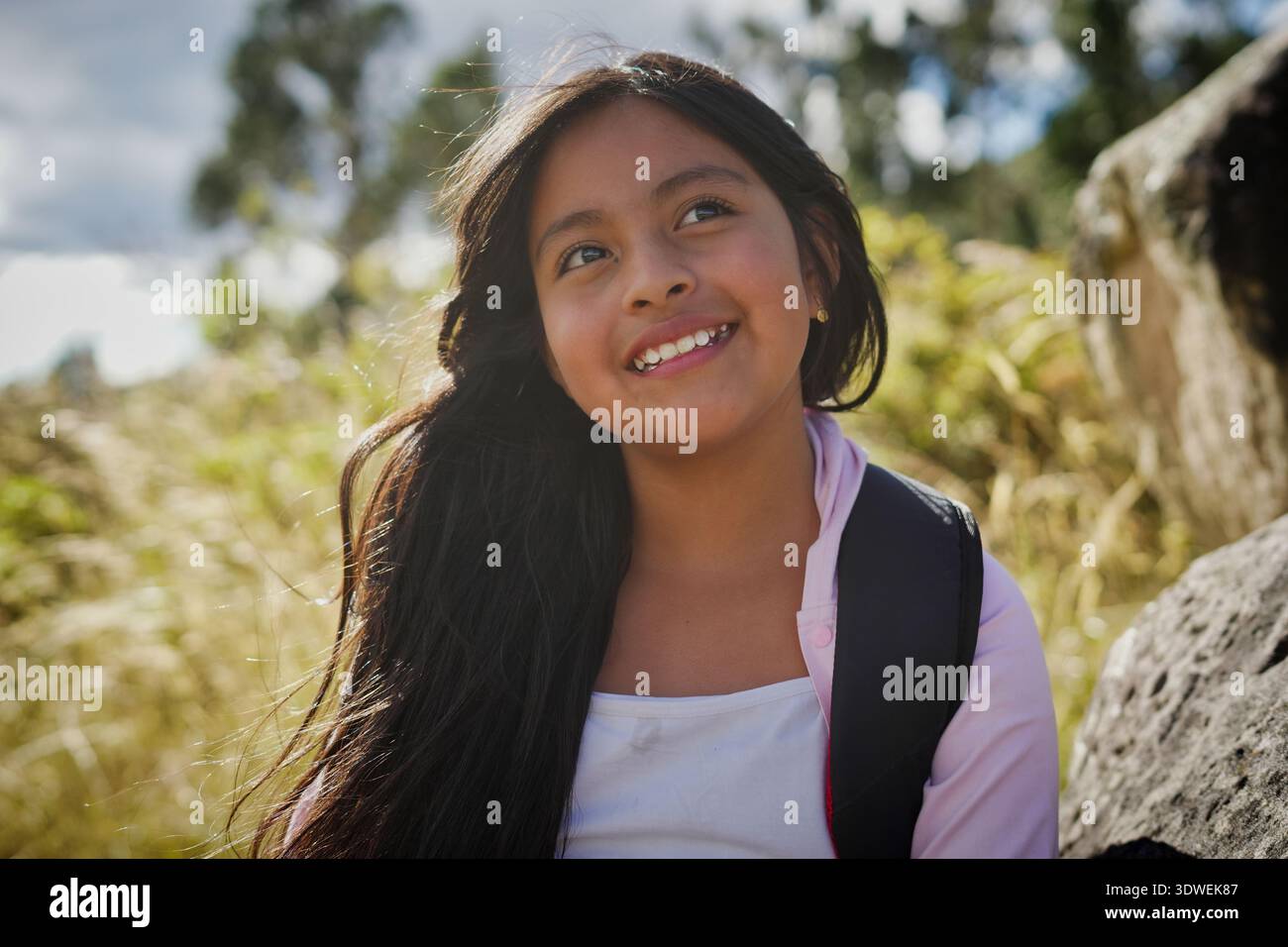 Joyeux élève d'école primaire latino-américaine souriant et regardant loin, profitant d'une excursion dans la nature, entouré de plantes et d'arbres vibrants sur Banque D'Images