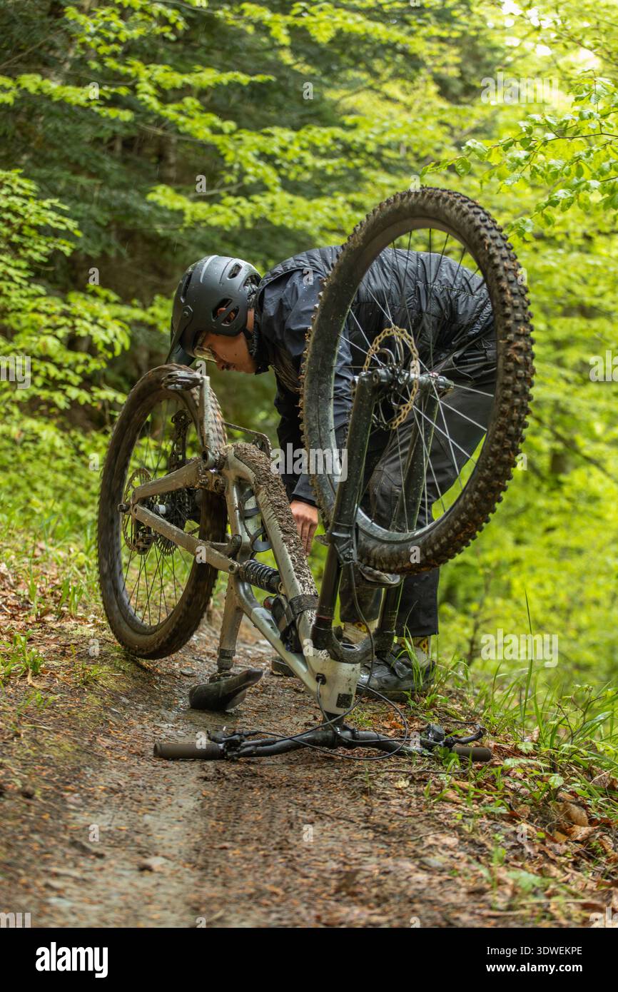 Un homme répare son VTT sur un chemin de terre dans les Pyrénées verdoyantes et luxuriantes. Le sentier est entouré d'un feuillage dense, créant une atmosphère extérieure sereine Banque D'Images