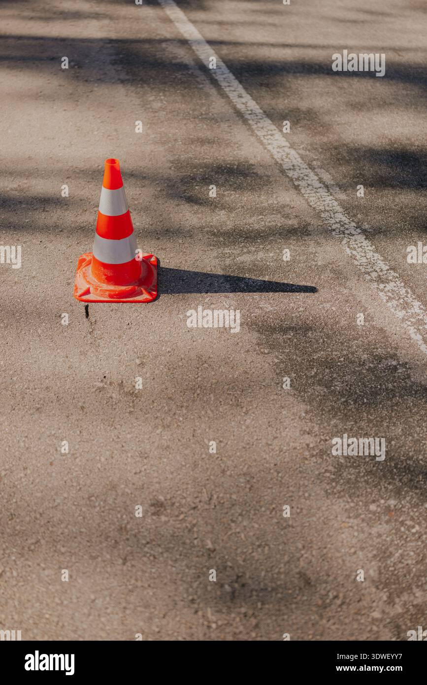 Un cône de circulation orange solitaire se tient sur une route asphaltée, projetant une ombre. La route présente une ligne blanche, faisant allusion à une construction ou à l'entretien A. Banque D'Images