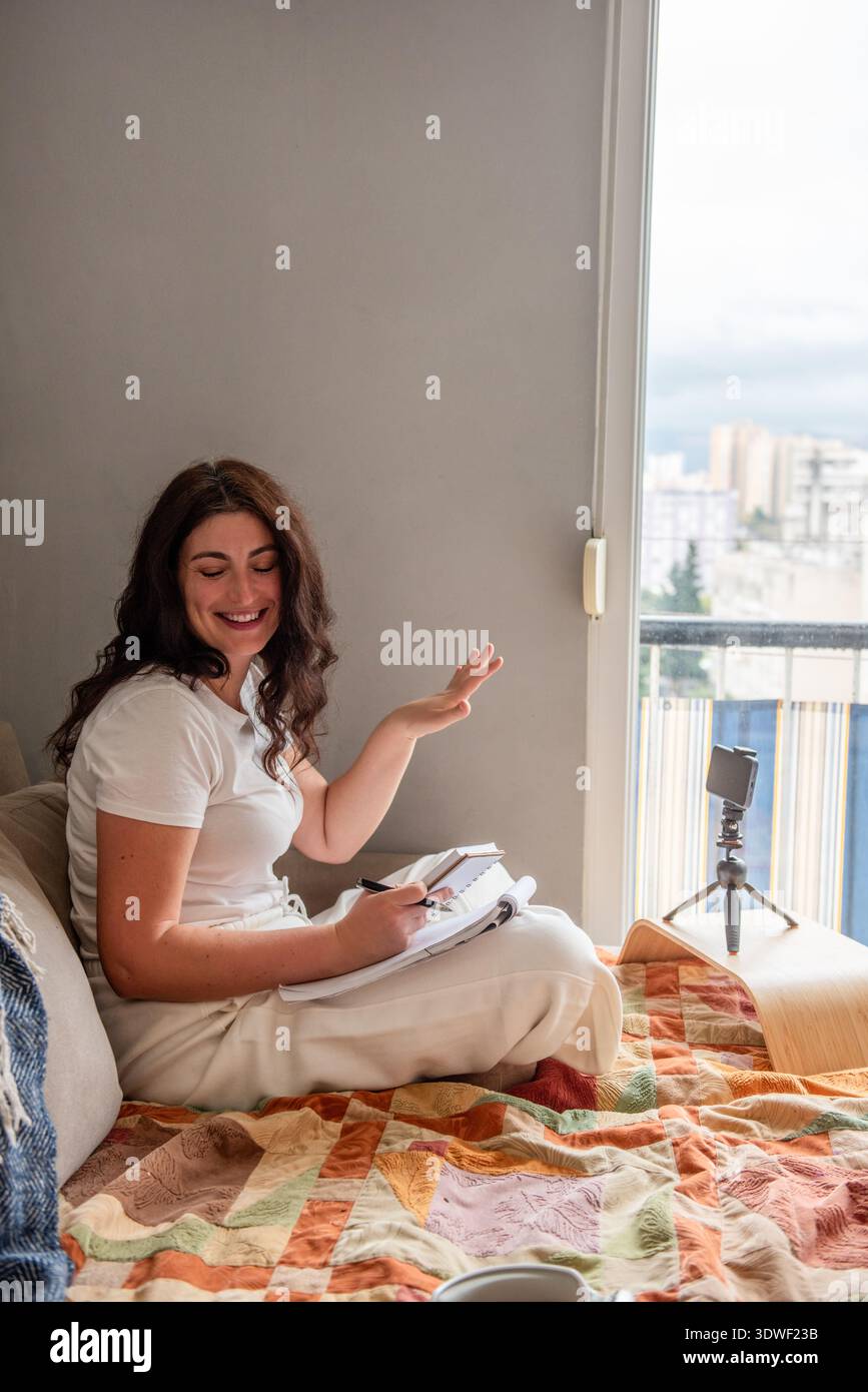 Une blogueuse diffuse du contenu depuis son domicile, à l'aide d'un smartphone. Elle est assise confortablement, engageant avec son public dans un cadre confortable. Banque D'Images
