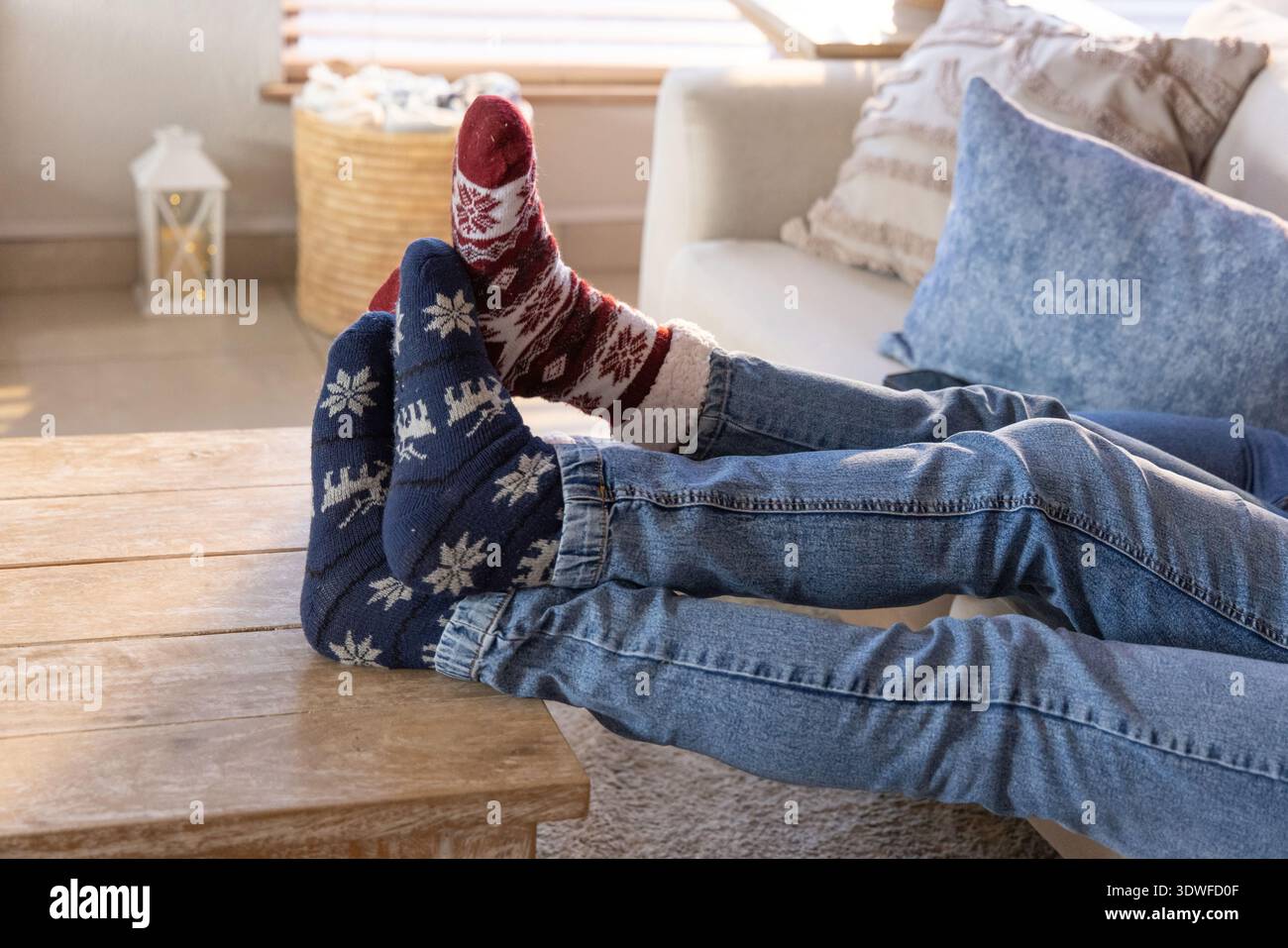 Couple incliné sur le canapé à la maison avec les jambes sur la table en bois, portant des jeans et des chaussettes à motifs Banque D'Images