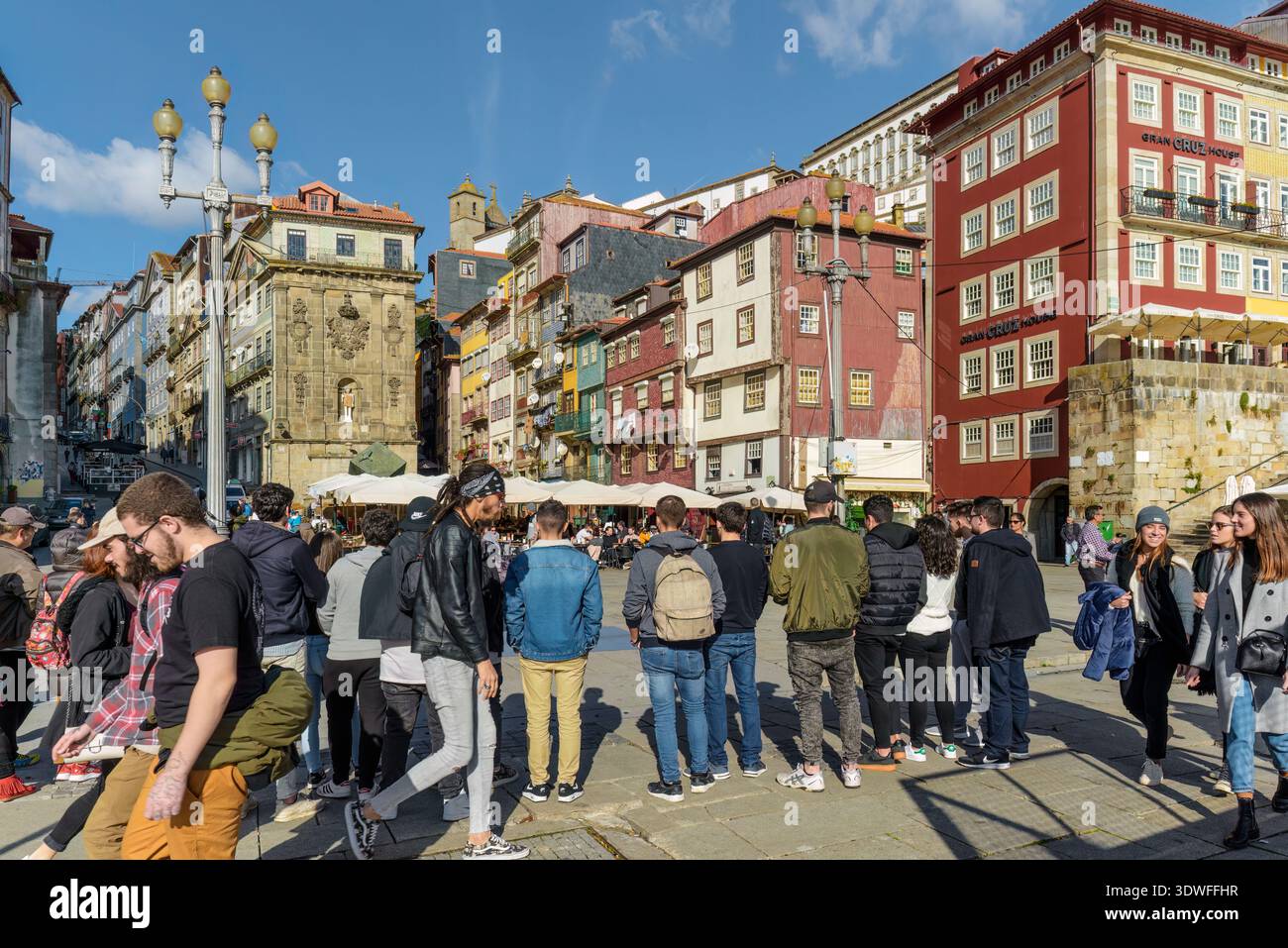 Animée Praça da Ribeira à Porto, Portugal, avec des bâtiments historiques colorés et des cafés en plein air sous un ciel bleu clair. Banque D'Images