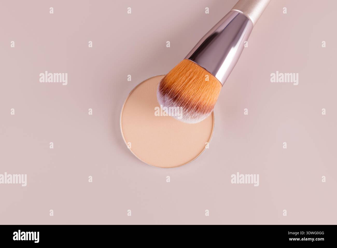 Un gros plan d'un compact de poudre cosmétique pour le visage accompagné d'un pinceau de maquillage sur un fond rose doux. Parfait pour illustrer la beauté, les soins de la peau, et c Banque D'Images
