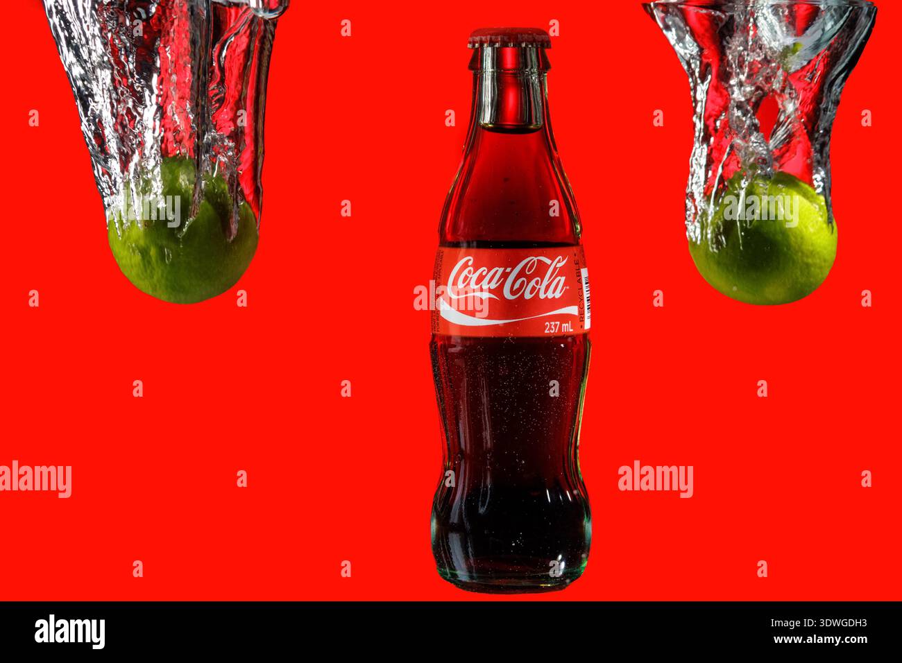 Bouteille de Coca-Cola centrée avec des citrons verts éclaboussant dans l'eau. Banque D'Images