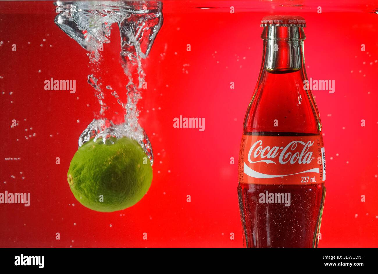 Bouteille de Coca-Cola à côté de chaux éclaboussant dans l'eau. Banque D'Images