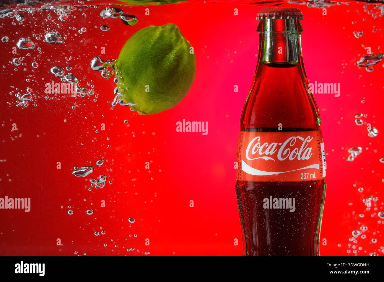 Bouteille de Coca-Cola à côté de chaux éclaboussant dans l'eau. Banque D'Images