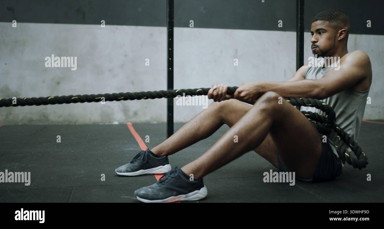 Homme, cordes de combat et entraînement sur le sol de gymnastique avec traction, entraînement intense et résilience avec défi. Personne, forme physique et puissance avec la respiration Banque D'Images