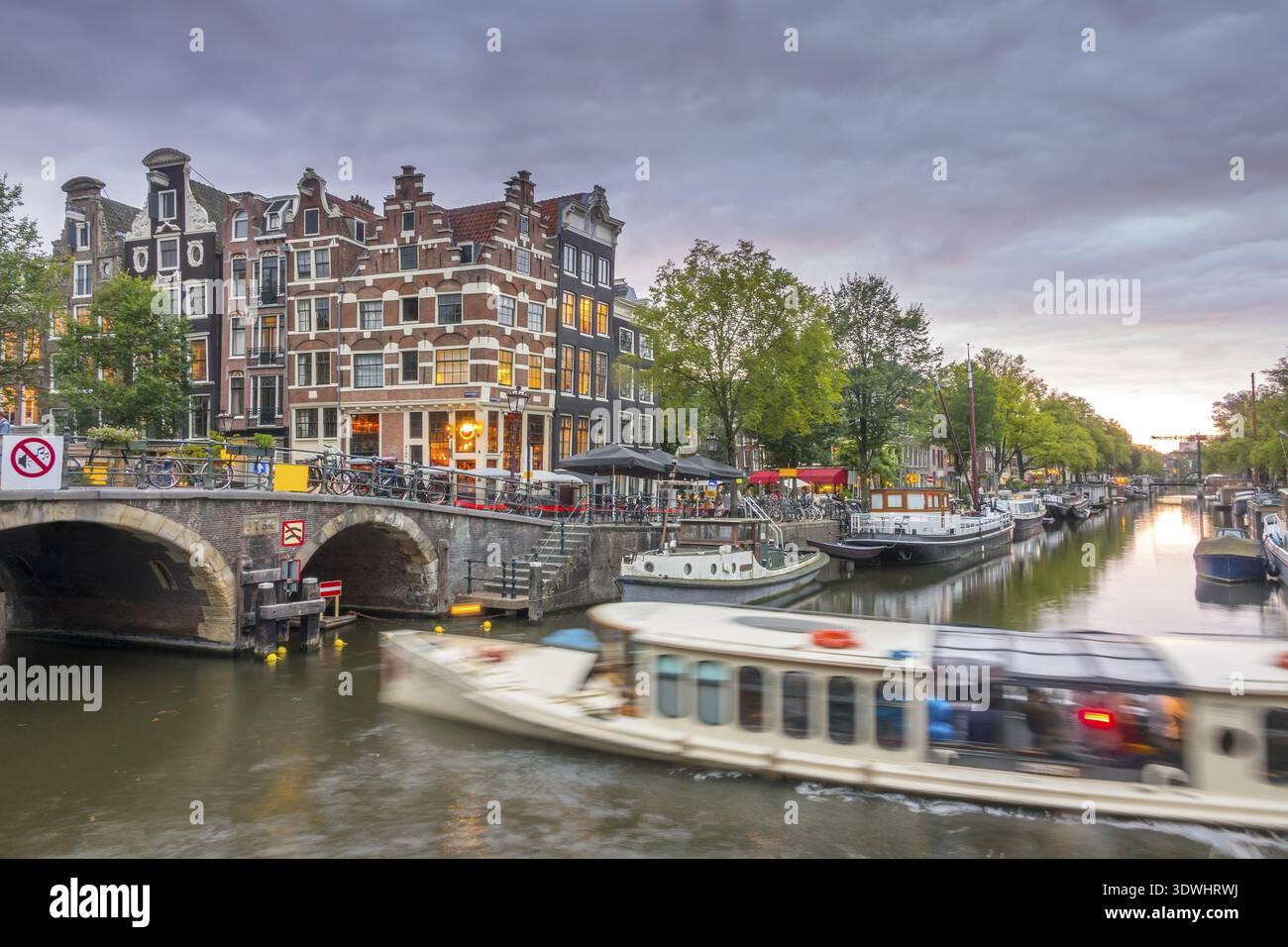 Pays-Bas. Crépuscule nuageux sur le canal d'Amsterdam. Les Péniche et les bateaux sont amarrés. Réflexion dans l'eau des maisons traditionnelles et d'un pont Banque D'Images