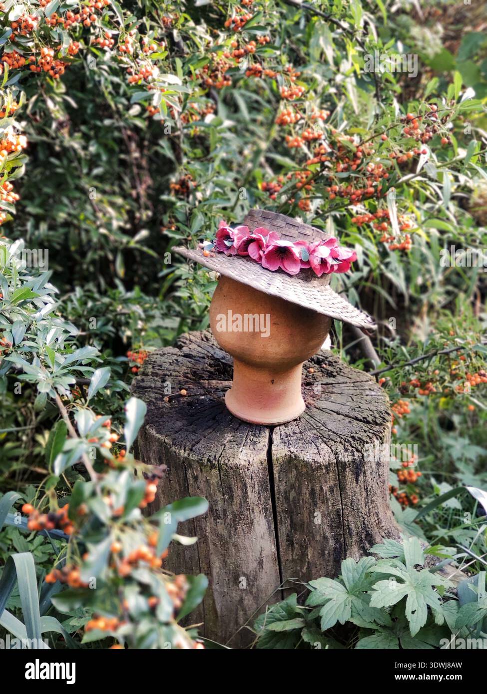 dans les buissons avec des baies oranges sur une souche, il y a un arbre en argile sur lequel est habillé un chapeau de paille avec des fleurs roses. rustique vibe mannequin rustique boho Banque D'Images