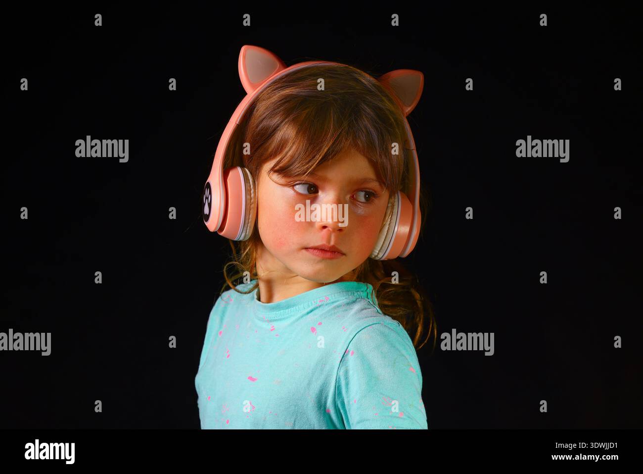 Fille profitant de la musique avec des écouteurs circum-aural dans un décor moderne sombre, exprimant la joie de l'enfance, la détente et une connexion naturelle à l'audio numérique Banque D'Images