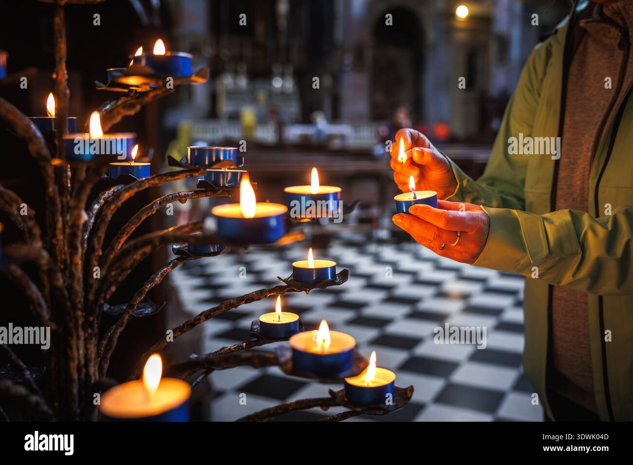 Femme allumant des bougies de prière à l'intérieur de l'église. Rituel spirituel de culte chrétien et de foi à Dieu Banque D'Images