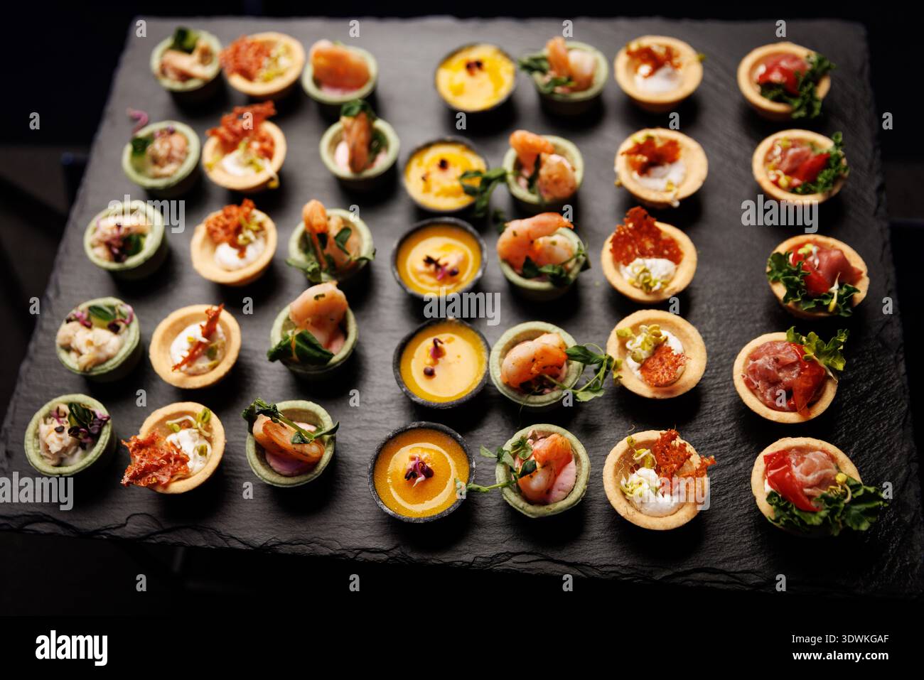 Une variété de petites tartes salées et canapés disposés en rangées pour un événement. La sélection comprend des crevettes, de la mousse et des garnitures de légumes. Banque D'Images