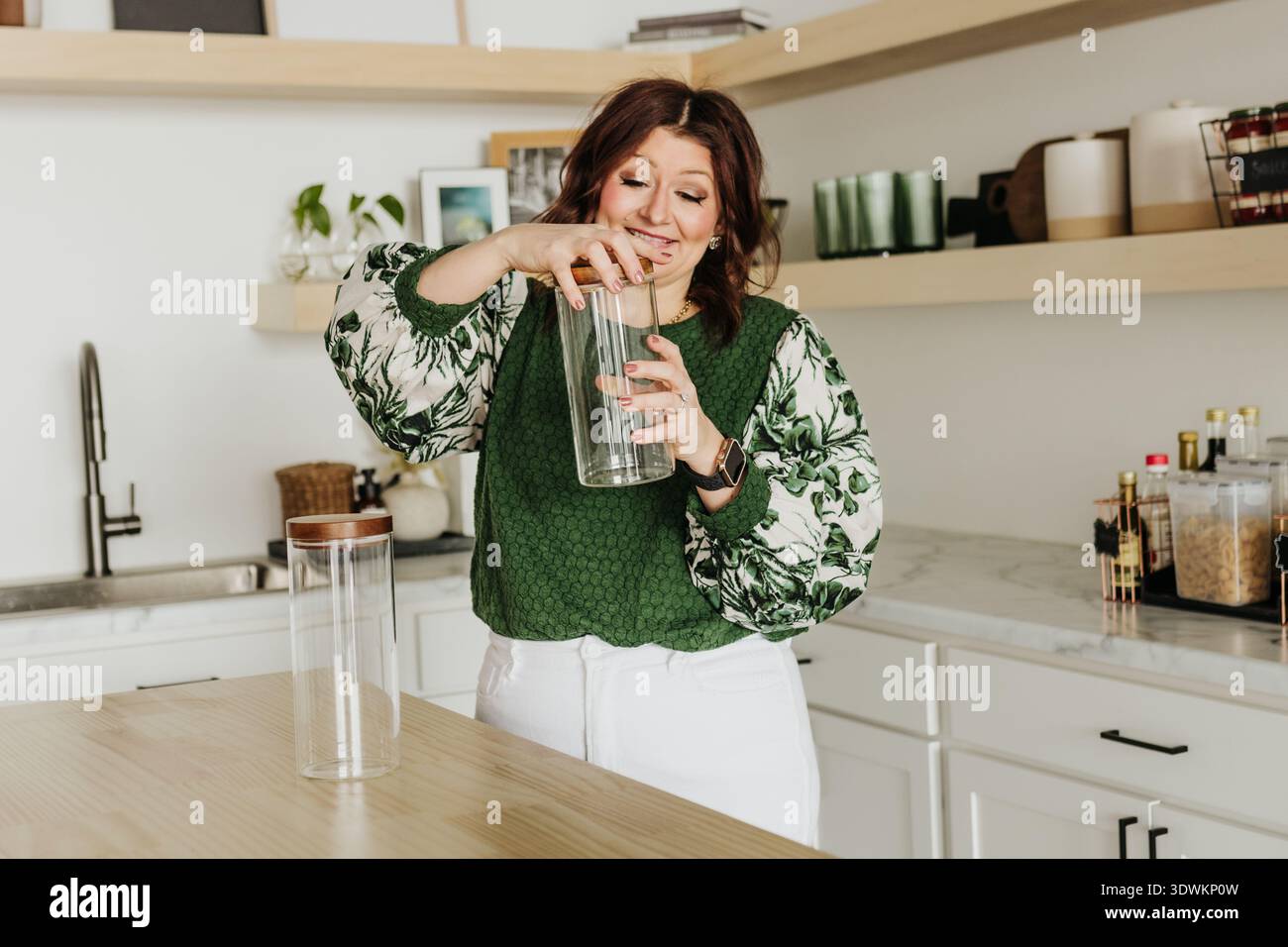 Femme visse le couvercle sur le bocal en verre vide tout en se tenant debout dans la cuisine Banque D'Images