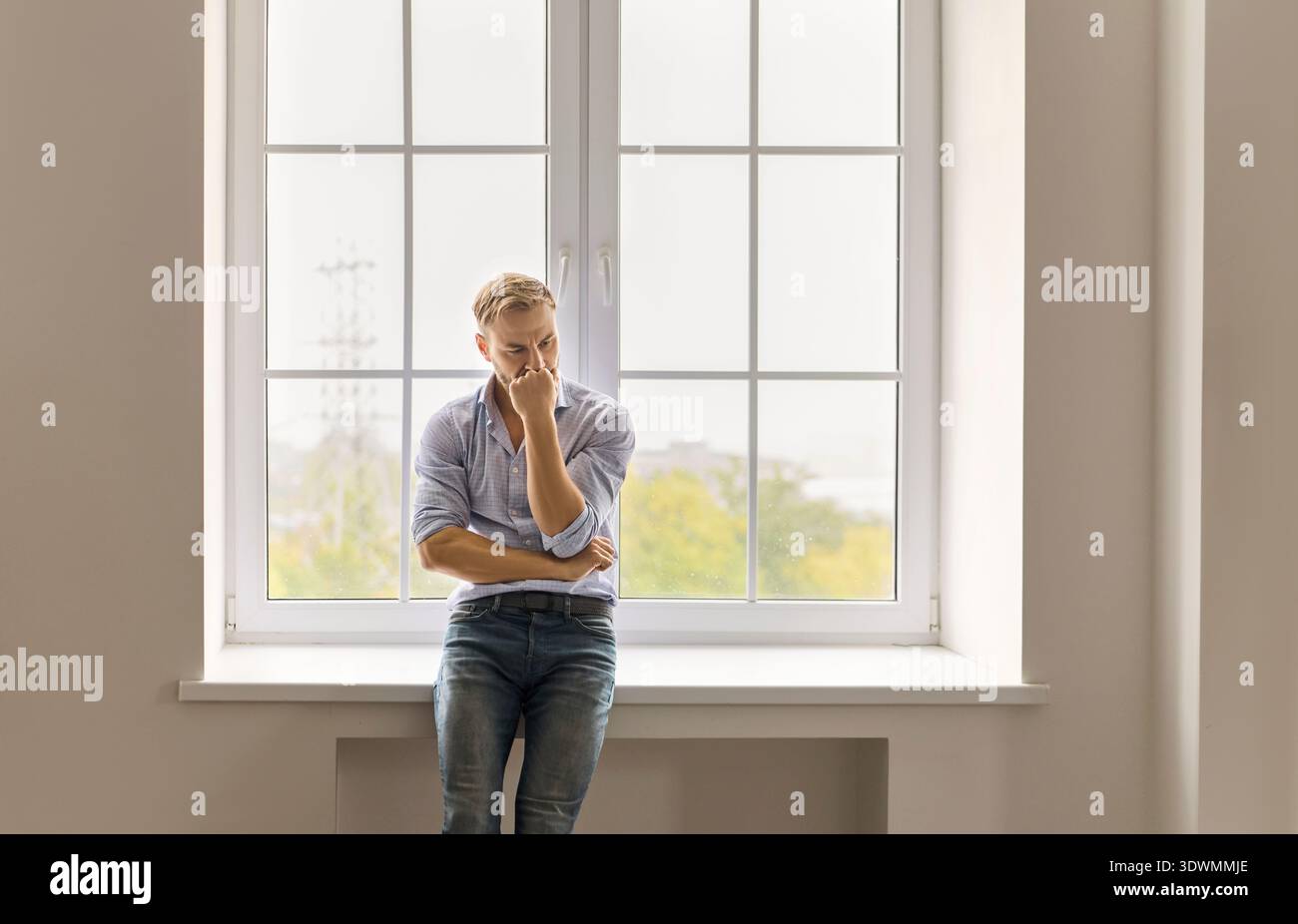 Homme concerné par la grande fenêtre pensant au stress, à l'anxiété et à la santé mentale Banque D'Images