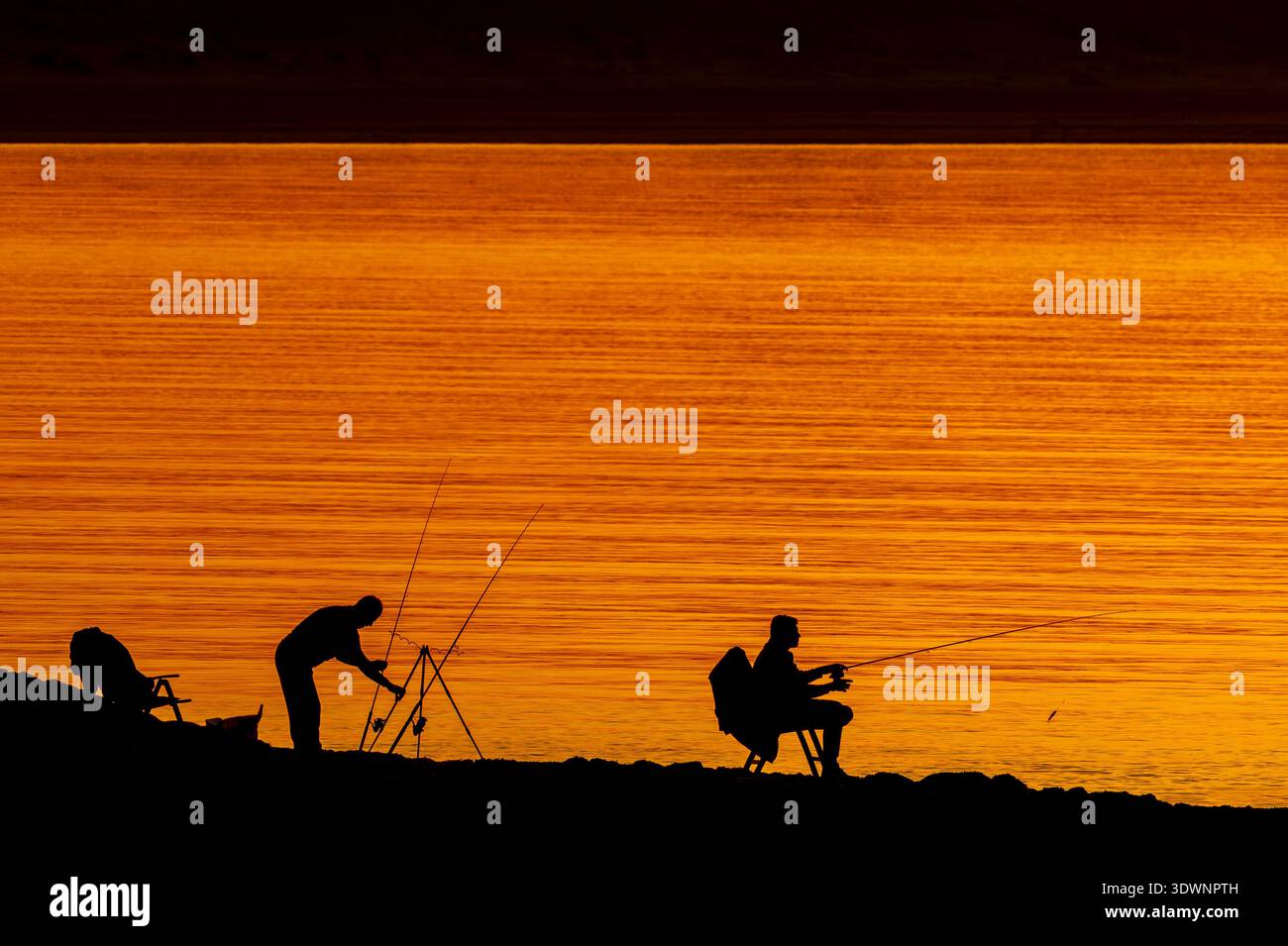 Silhouette de deux pêcheurs récréatifs / pêcheurs avec plusieurs cannes à pêche à la ligne au coucher du soleil Banque D'Images
