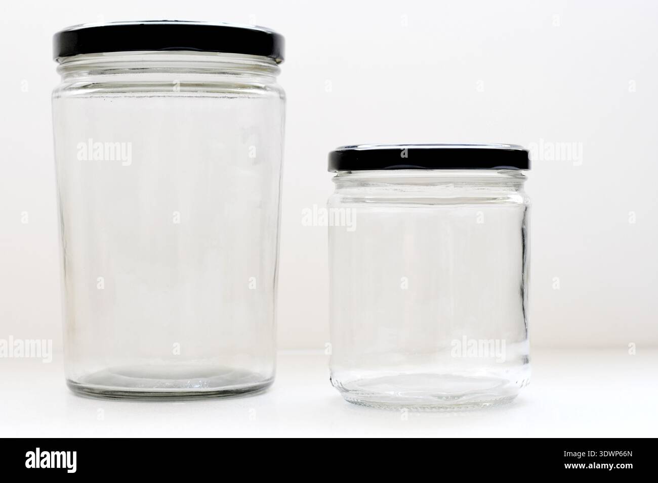 Grandes et petites bouteilles vides en verre transparent avec des bouchons noirs placés sur une table blanche avec un fond blanc propre, idéal pour les cosmétiques Banque D'Images