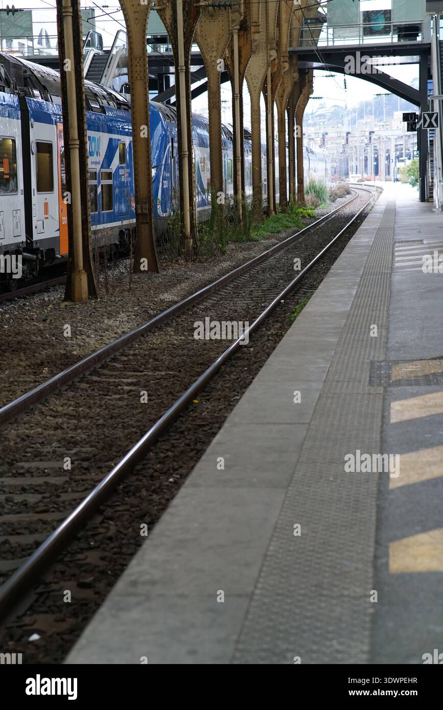 Plate-forme historique ensoleillée à la Gare de Nice ville avec d'élégantes colonnes dorées, un auvent orné et un train régional bleu élégant Zou attendant sur les rails. Banque D'Images