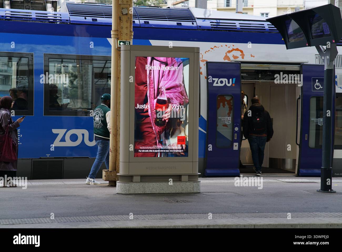 Le panneau publicitaire accrocheur de la gare de Nice promeut le « plaisir d'hiver » de Zou avec une silhouette joyeuse en veste rouge dégustant une boisson chaude Banque D'Images