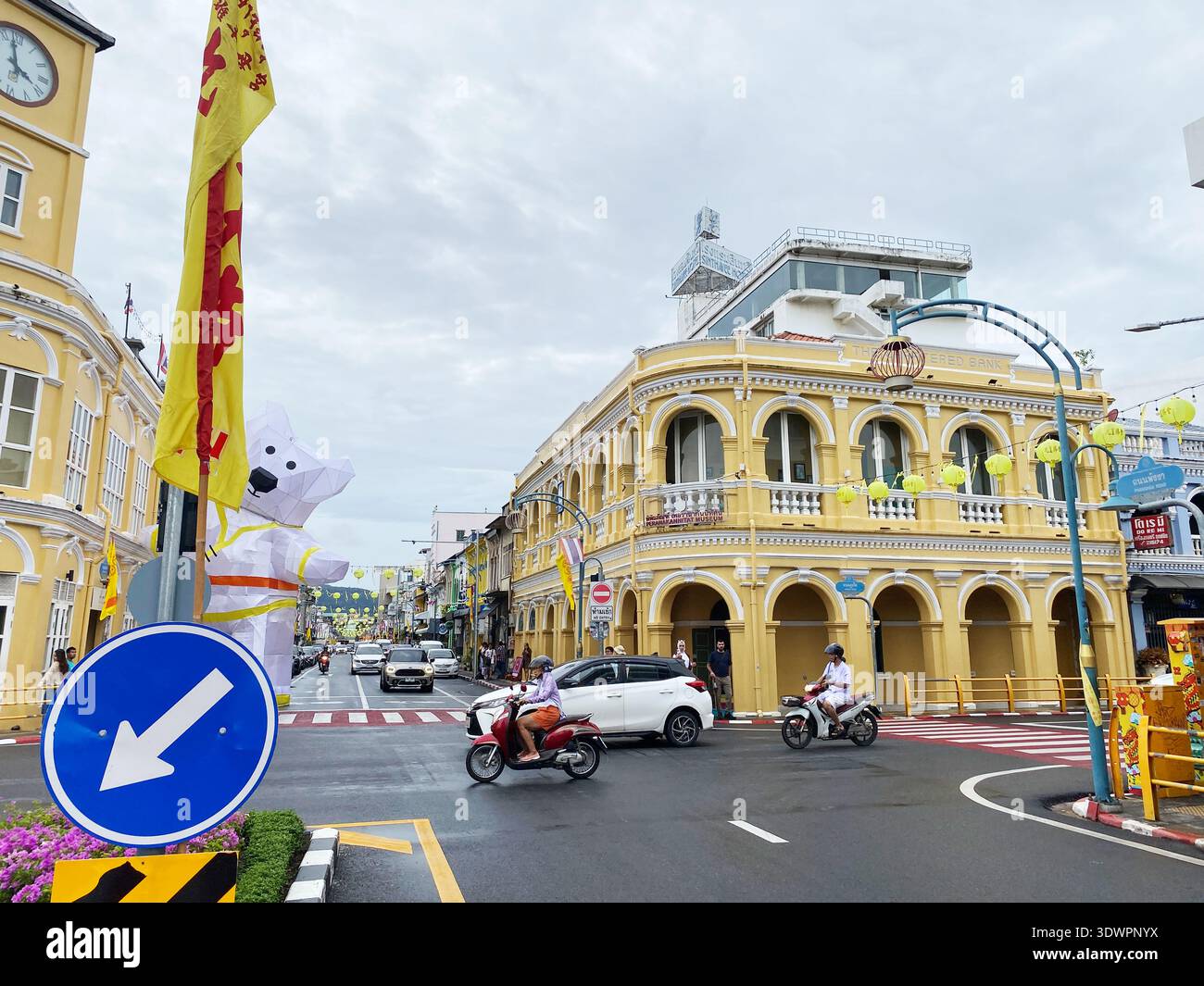 Phuket, Thaïlande - 28 octobre 2025 : bâtiments historiques dans la vieille ville de Phuket avec des façades jaunes, des panneaux de signalisation et des véhicules sur la route sous un nuage Banque D'Images