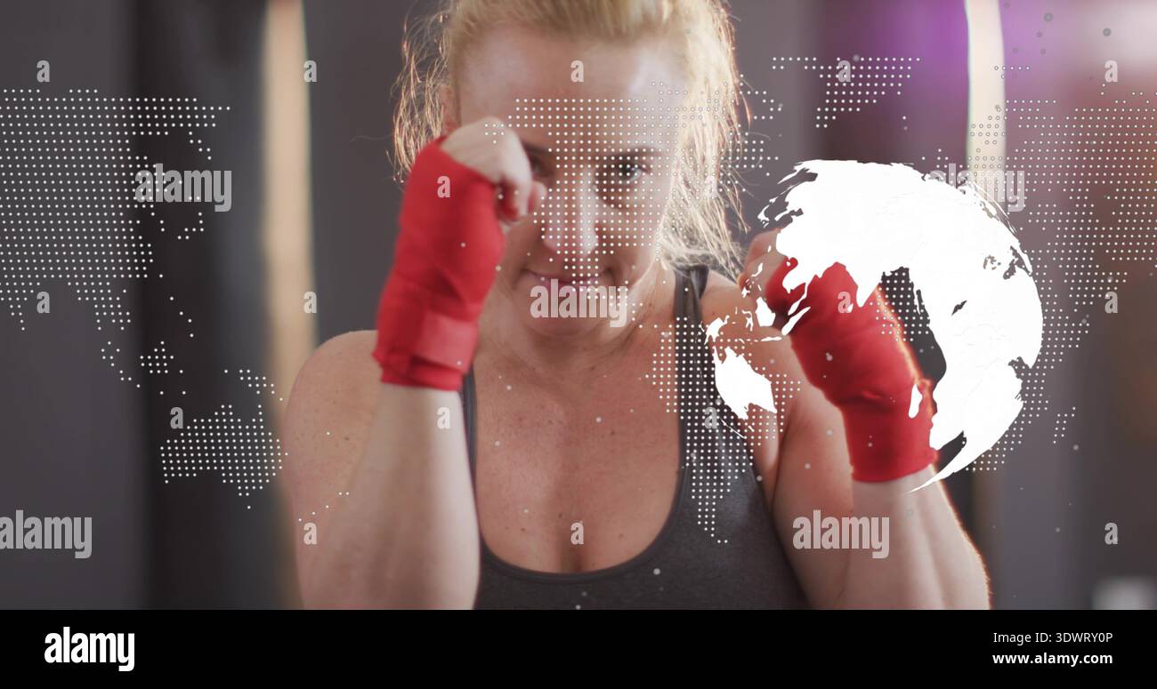 Boxer de femme de formation levant les poings dans le gymnase, portant un réservoir sombre et des enveloppements de main rouges, carte ou globe overla Banque D'Images