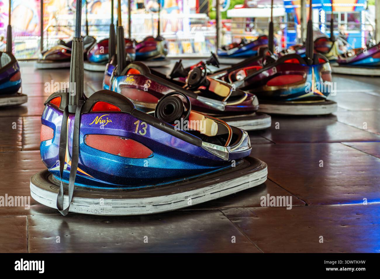 Voitures tamponneuses colorées dodgem lors d'une promenade au champ de foire, avec une voiture bleue et violette 'Ninja' numérotée 13 au premier plan. Banque D'Images
