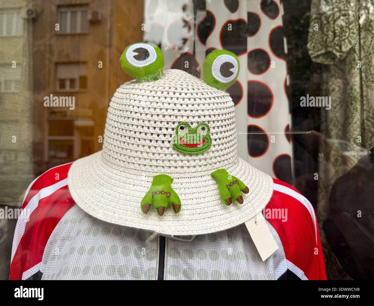 Chapeau d'enfants tricoté blanc avec décoration drôle de grenouille affichée sur mannequin dans la vitrine du magasin de vêtements. Accessoire de mode ludique, style d'enfance Banque D'Images