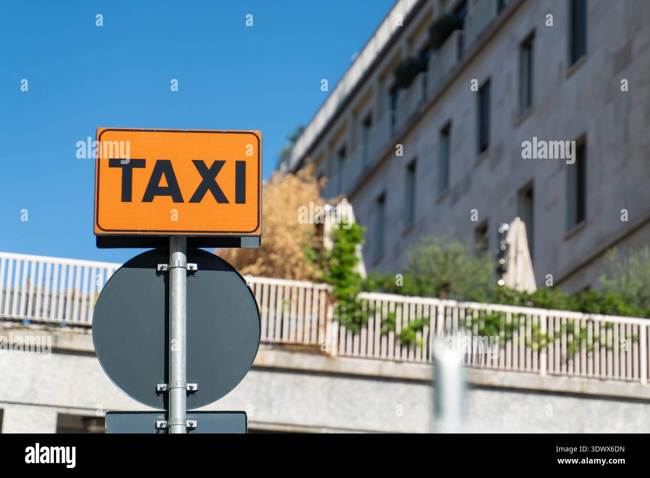Un panneau de taxi rectangulaire s'élève contre une façade de ville avec des balcons et des plantes. La scène montre les infrastructures urbaines quotidiennes sous la lumière chaude du soleil. Banque D'Images