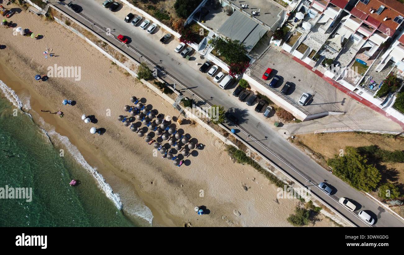 Vue aérienne de dessus de la plage de Vrahos, Grèce. Drone shot de la mer Ionienne turquoise, côte sablonneuse avec des parasols, voitures garées et route côtière en été. Banque D'Images