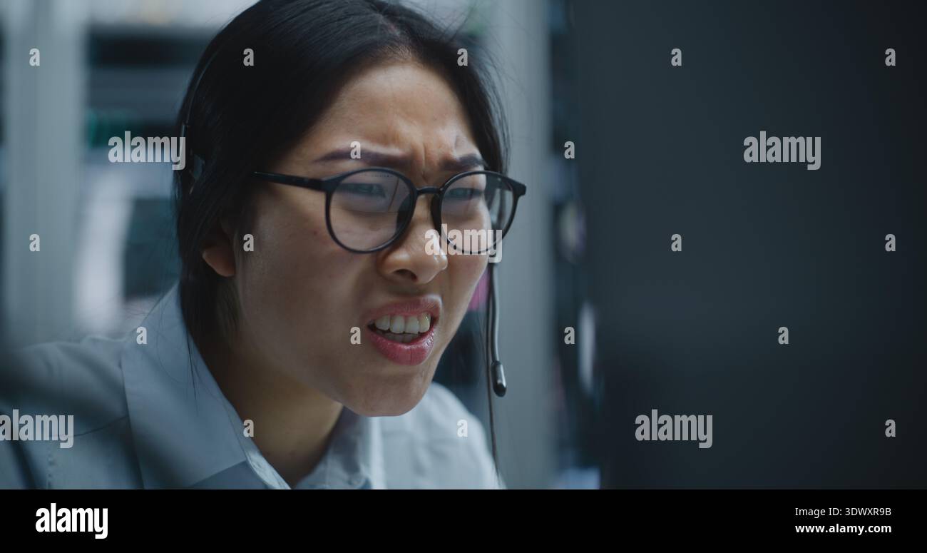 La négociante asiatique reçoit un appel via le casque tout en surveillant les données financières dans Modern Stock Office. Femme écoute Bad News à propos de la performance du marché, expression déplace l'inquiétude et la détresse. Banque D'Images