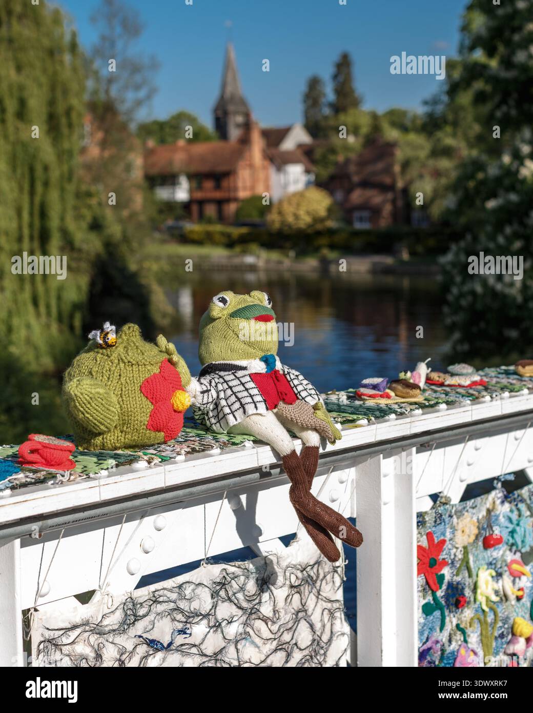 Art de bombardement de fil mettant en vedette la grenouille tricotée Mr Toad sur la rambarde du pont au-dessus de la Tamise et vue sur l'église St Mary à Whitchurch-on-Thames Banque D'Images